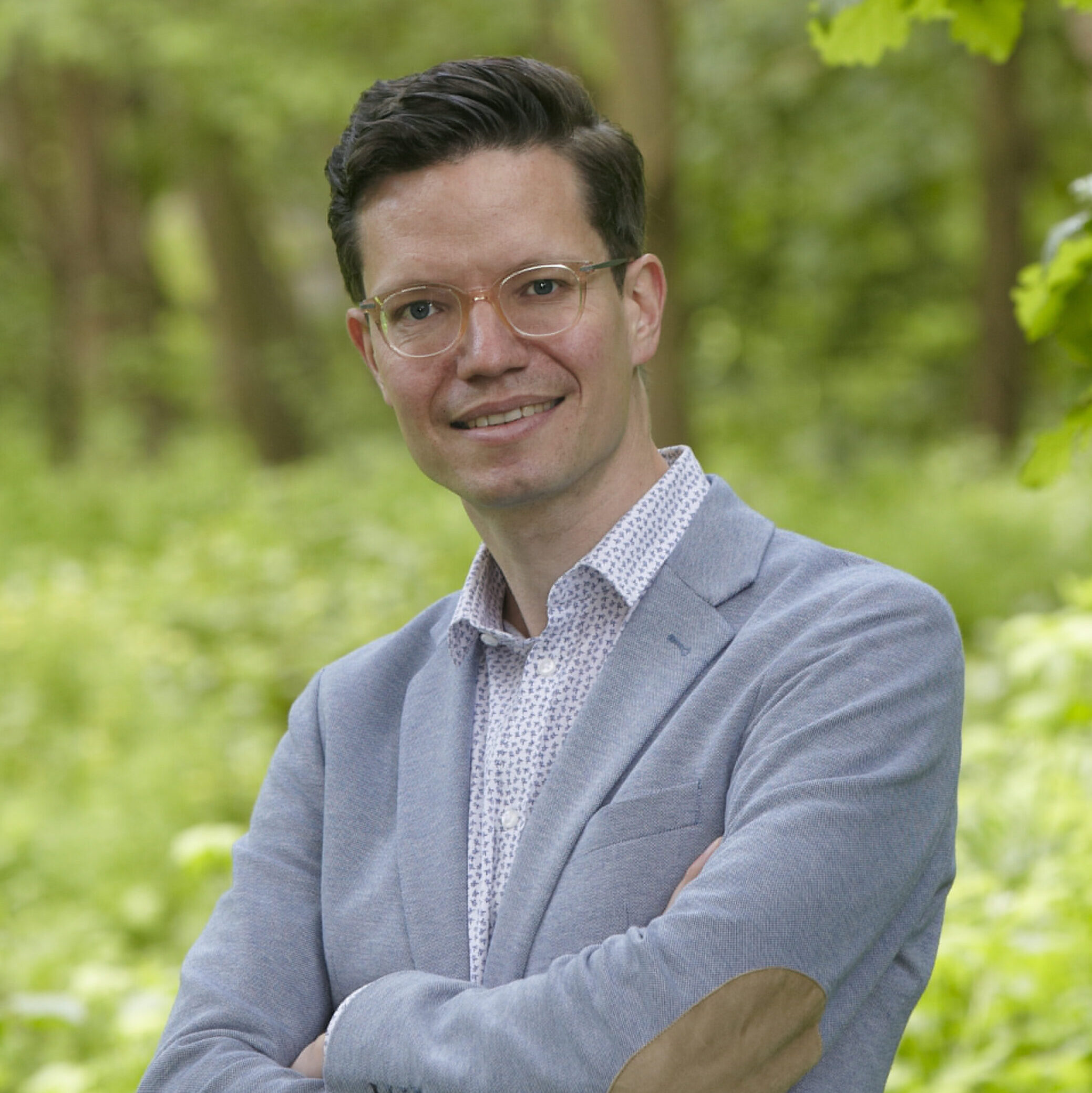 Professor Holger Cramer in grey blazer with glasses stands smiling with arms crossed